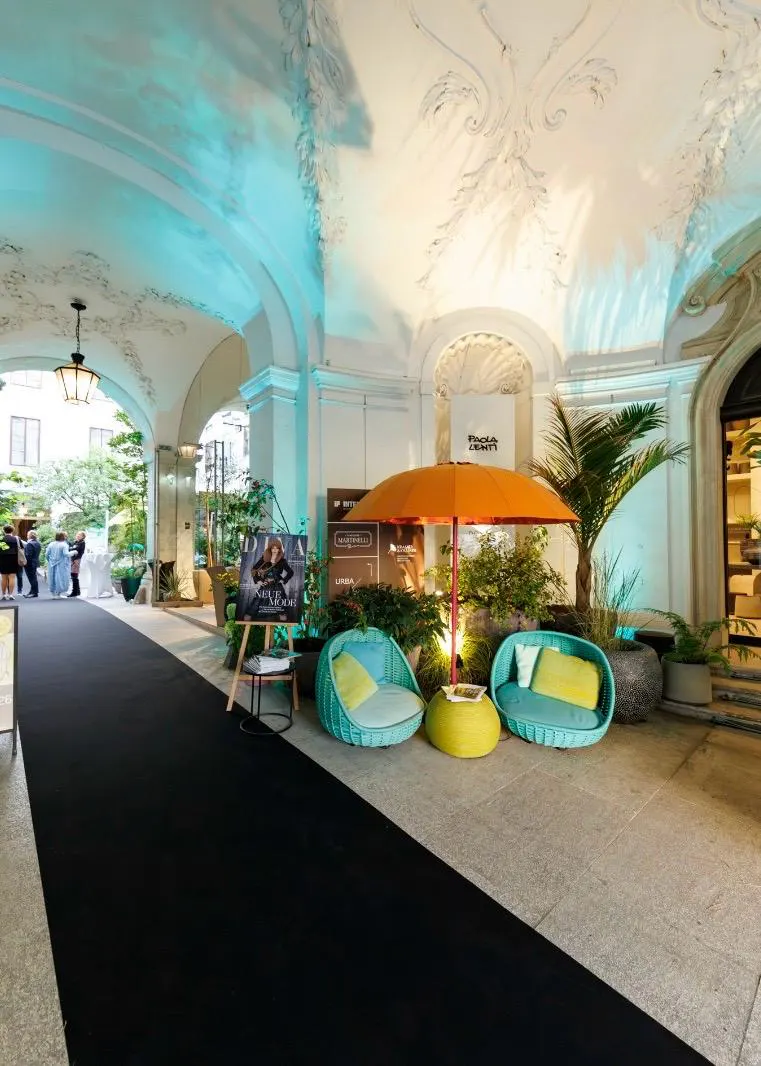 Exklusives Event-Setup im historischen Palais Ferstel in Wien mit schwarzem Teppich, türkisfarbenen Lounge-Sesseln unter einem orangen Sonnenschirm und einem Aufsteller des Design District.