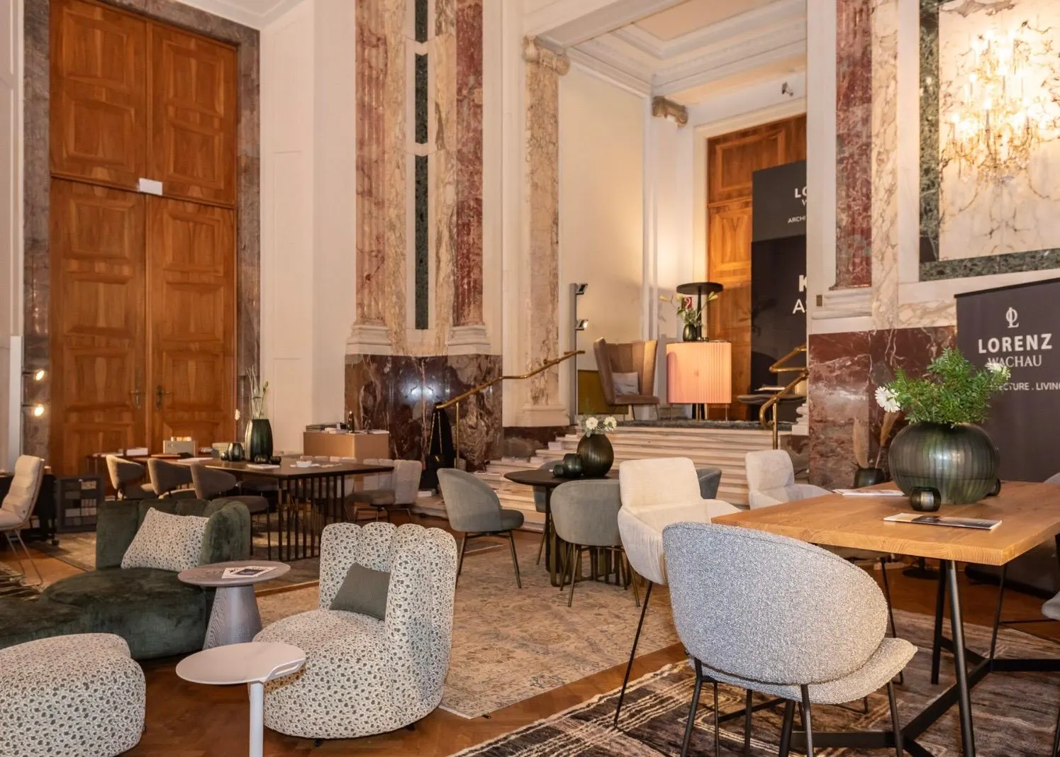 Ausstellungsfläche beim Design District 2026 in der Wiener Hofburg mit modernen Sesseln, Tischen und historischen Marmorsäulen.