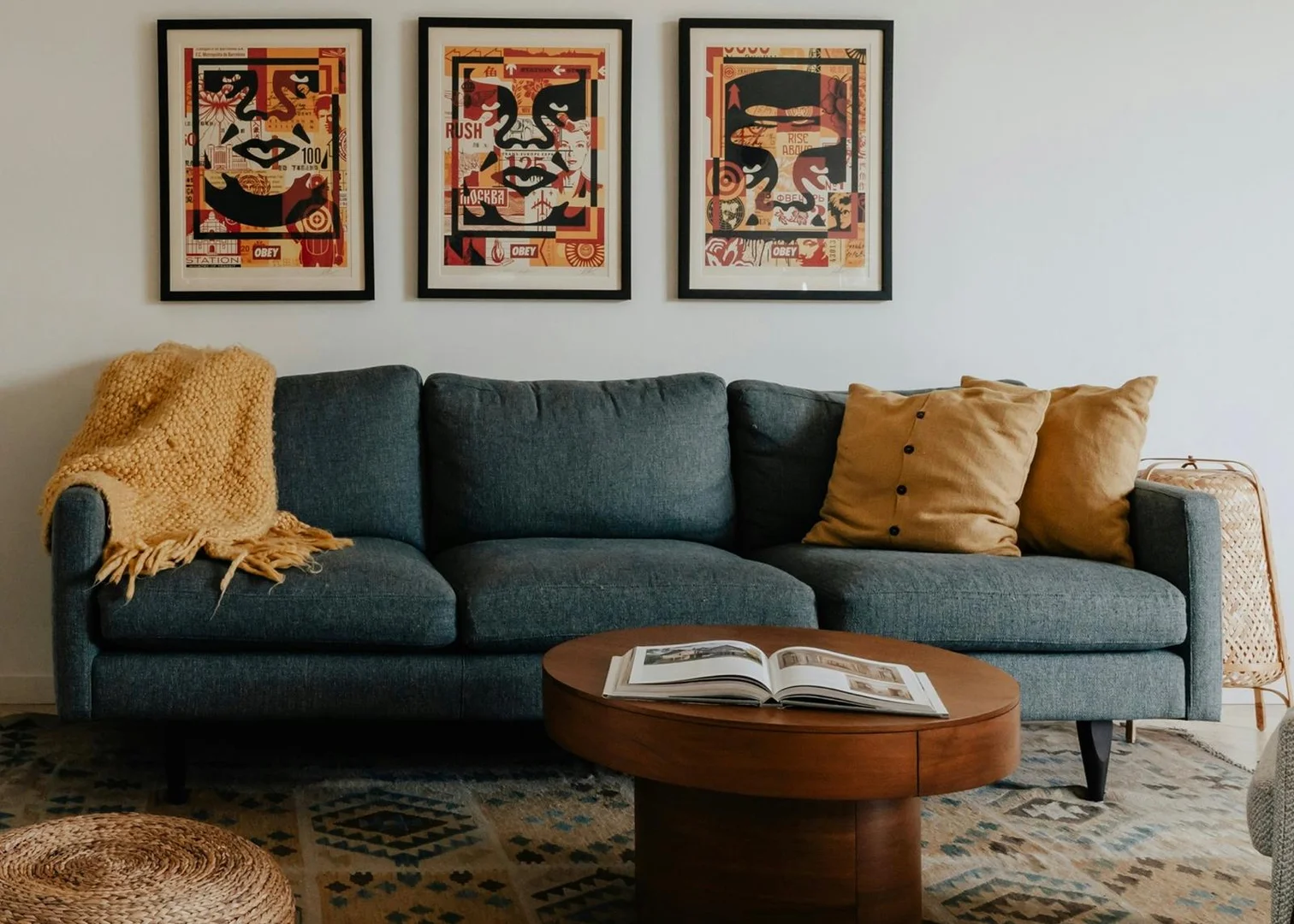 Slow Living Wohnzimmer mit blauem Sofa und Holzmoebeln einrichten Gemütliche Sitzecke im Slow Living Stil mit einem dunkelblauen Sofa, Holz-Couchtisch, gemustertem Teppich und drei gerahmten Bildern an der Wand.