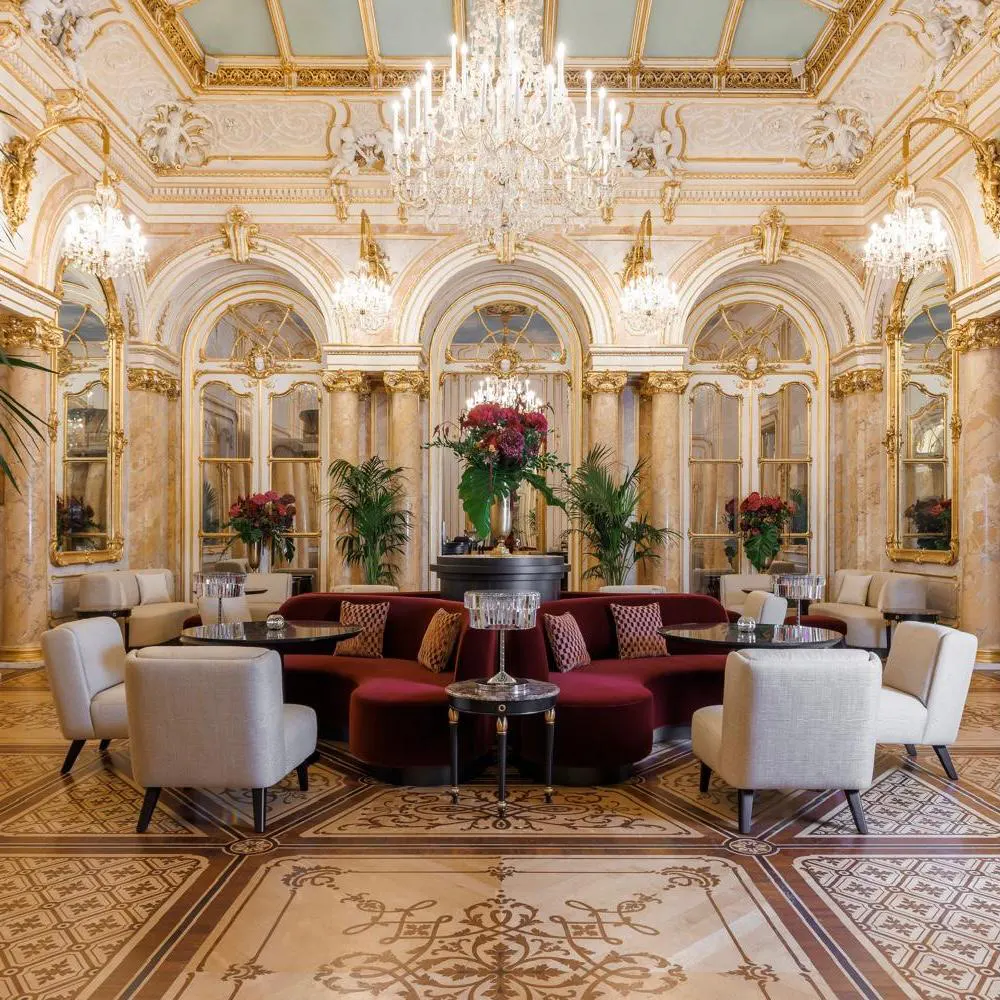 Prunkraum und Restaurant im Palais Coburg Wien Prunkvoller historischer Saal im Luxushotel Palais Coburg in Wien mit weißen Sesseln, dunkelroten Sofas, Kristallleuchtern und Marmorsäulen.